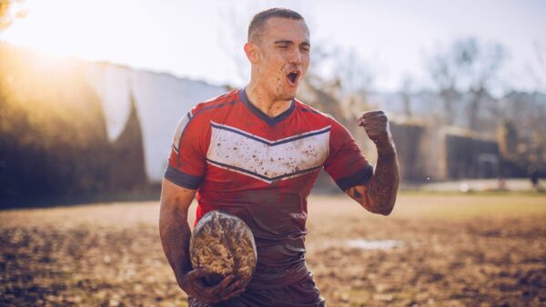 A mud covered athlete standing in a field celebrates a victory.
